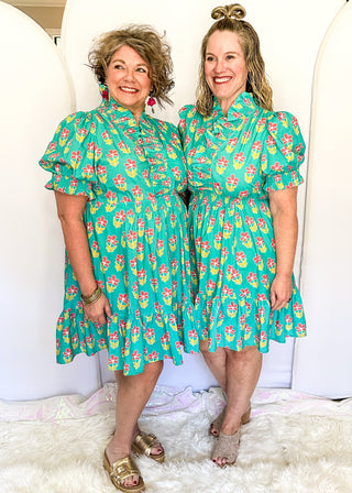Mint green floral dress with colorful pink flowers, featuring short puff sleeves, ruffled neckline, smocked waist, and flowy skirt.