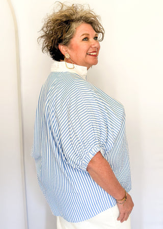 Striped seersucker top in light blue and white with short sleeves, relaxed fit, and split neckline.
