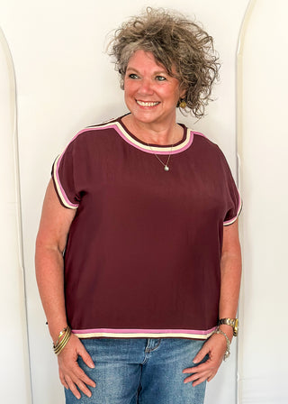 woman standing in Merlot top with pink and white contrast detail. 