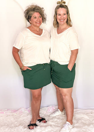 Two women wearing emerald skorts with pockets and white tees.