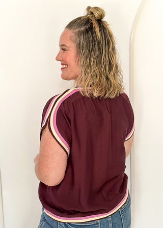 woman standing in Merlot top with pink and white contrast detail. 