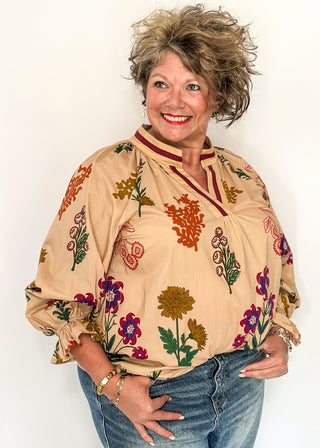 Beige top with v-neckline, contrast trim, and vibrant floral design.