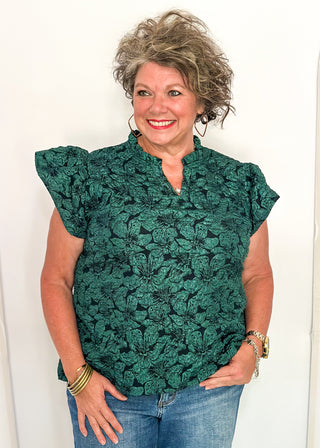 woman wearing forest green jacquard flutter sleeve blouse with a floral pattern