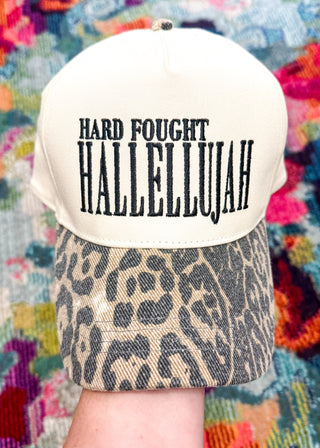 Snapback hat with "Hard Fought Hallellujah" embroidered in black with an animal print bill.