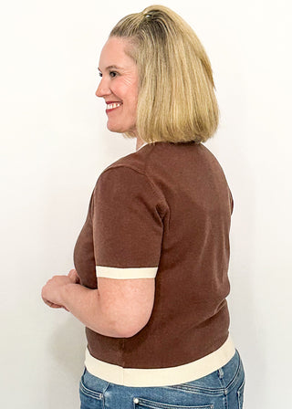side view of woman modeling a brown, short sleeve sweater with cream banding on sleeves, collar and hem.