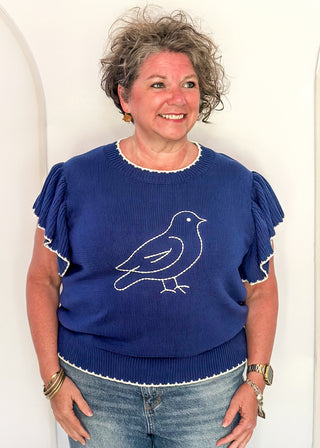 woman in blue ruffle sleeve sweater with white stitched bird