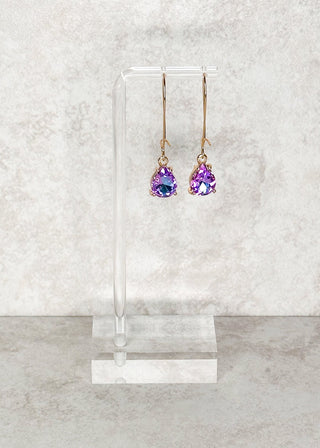 Teardrop gemstone dangle earrings in color shifting purples and blues. Displayed on a stand 