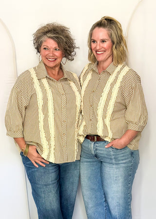Two women standing side-by-side wearing matching beige and brown vertically striped button-down shirts with cream lace-like ruffle accents down the front, paired with blue jeans.