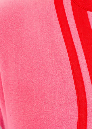 Close up of pink midi-length dress with contrast red trim at neckline and hem, short sleeves with elastic, relaxed fit, and pockets.