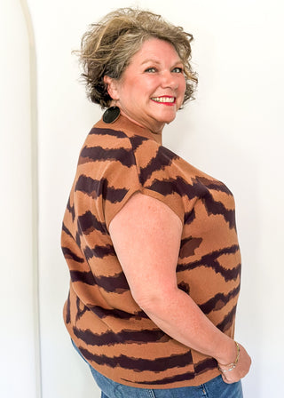 Woman wearing a brown and black tiger striped top with blue jeans against a white background