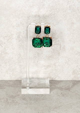 Emeral green gemstone dangle earrings displayed on a stand.
