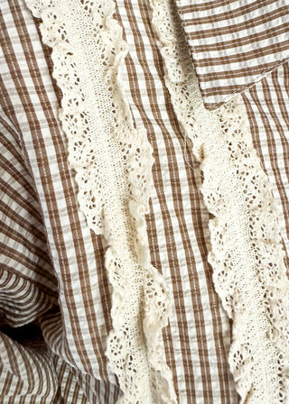 Close-up of a brown and cream gingham shirt with a cream lace ruffle detail down the front.