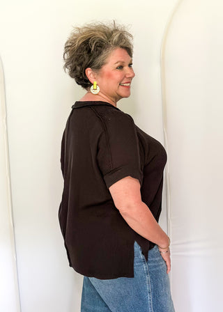 Woman wearing a brown top and blue jeans standing against a white background
