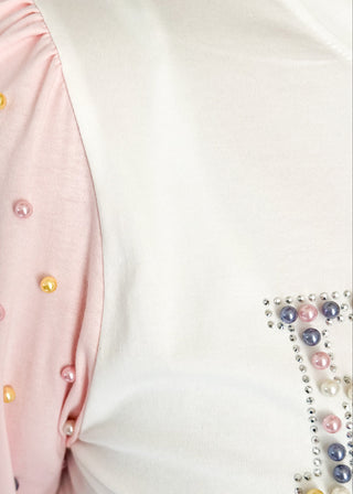 Off white short sleeve shirt with colorful embellished text and pink statement sleeves with decorative pearl studs.
