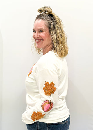 Light Ivory Long sleeve top with terracotta leaves and pink pumpkin patches sewn on the sleeves. "Thankful" chenille patches across the chest in pink and terracotta. 