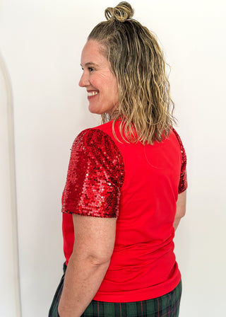 Woman wearing a red shirt with sequin sleeves against a white background