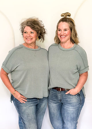 Two women wearing matching green tops and blue jeans against a white background
