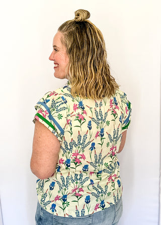Cream short sleeve floral top with blue, pink, and green flowers, featuring a split V-neckline with green trim and a relaxed fit.