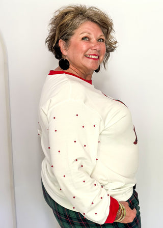 White long sleeve Christmas top with red neckline and cuffs, featuring a plaid Christmas tree appliqué with red sequin trim on the front. Red pearl accent the sleeves for a festive touch.”