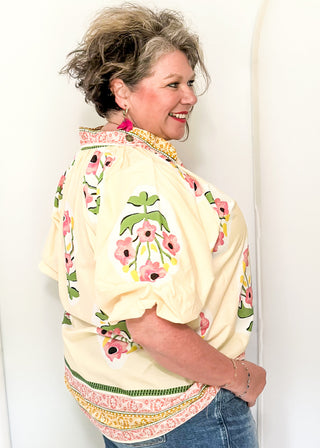 Women's short sleeve ecru top with pink floral bundles and decorative hem and collar. 