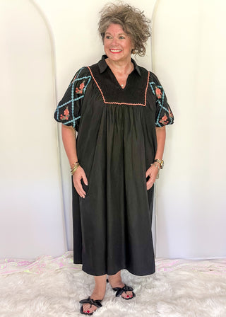 Women wearing a black midi dress with embroidered puff sleeves and a smocked bodice