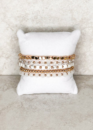 5 strand gold, clear and white bracelet set displayed on a stand 