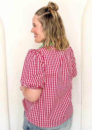 Women’s gingham blouse with decorative buttons and statement neckline detail.
