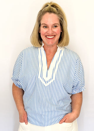 Striped seersucker top in light blue and white with short sleeves, relaxed fit, and split neckline.