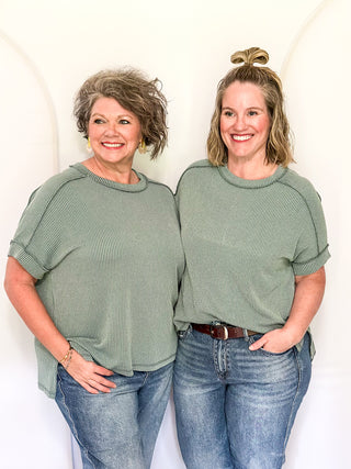 Two women wearing matching green tops and blue jeans standing against a white background