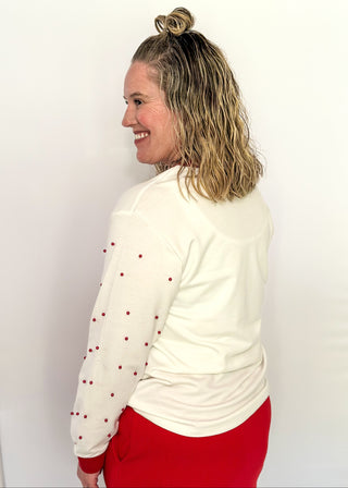White long sleeve Christmas top with red neckline and cuffs, featuring a plaid Christmas tree appliqué with red sequin trim on the front. Red pearl accent the sleeves for a festive touch.”