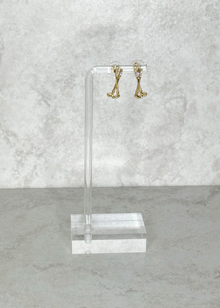 Gold golf club shaped earrings on a clear acrylic stand against a marble background