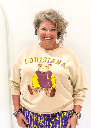 Tan long sleeve pull over with "LOUISIANA" in curved bold font above Benny the Bear in his Louisiana purple and gold letter jacket.  