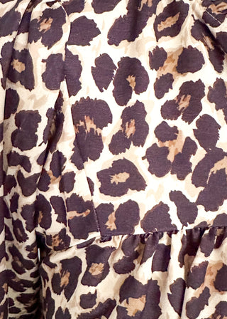Close-up of a leopard print fabric with dark brown and black spots on a warm beige background.