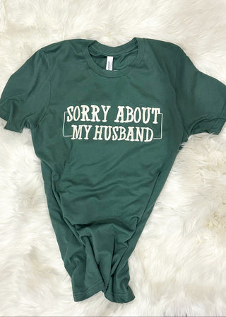 Green t-shirt with 'Sorry About My Husband' text on a white fluffy surface