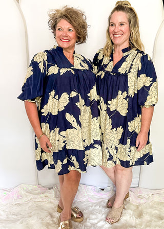 Two women wearing navy and white floral dresses standing in front of large white balloons.