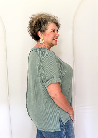 Woman wearing a green striped shirt and blue jeans standing against a white background