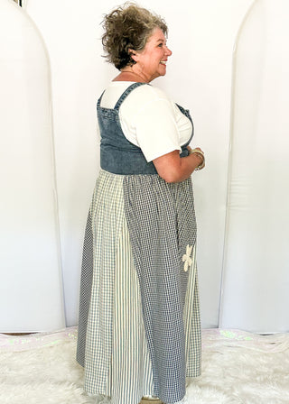 side view of woman modeling a denim overall style dress with gingham floral pattern.
