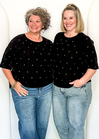 Two women wearing black sweaters with rhinestones, paired with jeans, standing together.