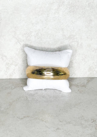 Gold colored bangle bracelet on a white cushion against a light gray background