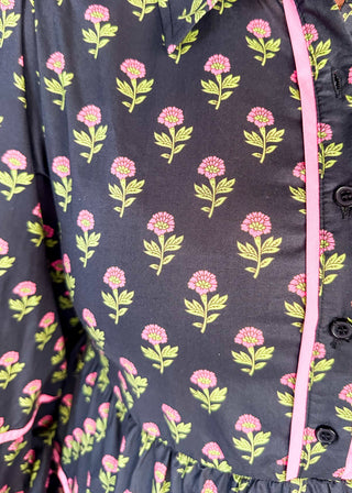 Long sleeve black knee-length dress. Pink and green floral design. Tiered with pink piping detail. Buttons on top.