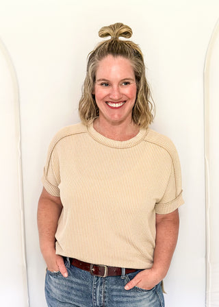 Woman wearing a beige ribbed sweater and blue jeans against a white background