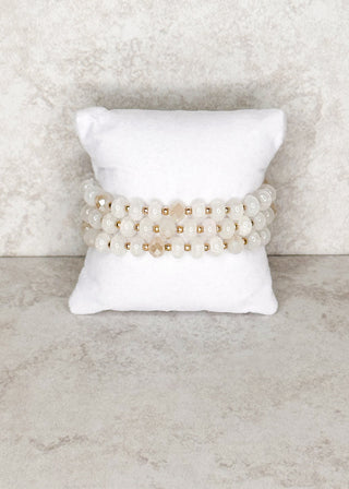 3 strand beaded milky white bracelets displayed on a stand 