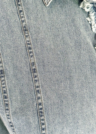 Denim button-down top with short sleeves, pointed collar, vertical stitched panels, and frayed raw-edge hem.