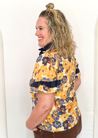 Bold Navy and golden blooms on this short sleeve top with navy ruffle detail on the sleeves, collar and 1/2 way down the front. Buttons up the front.
