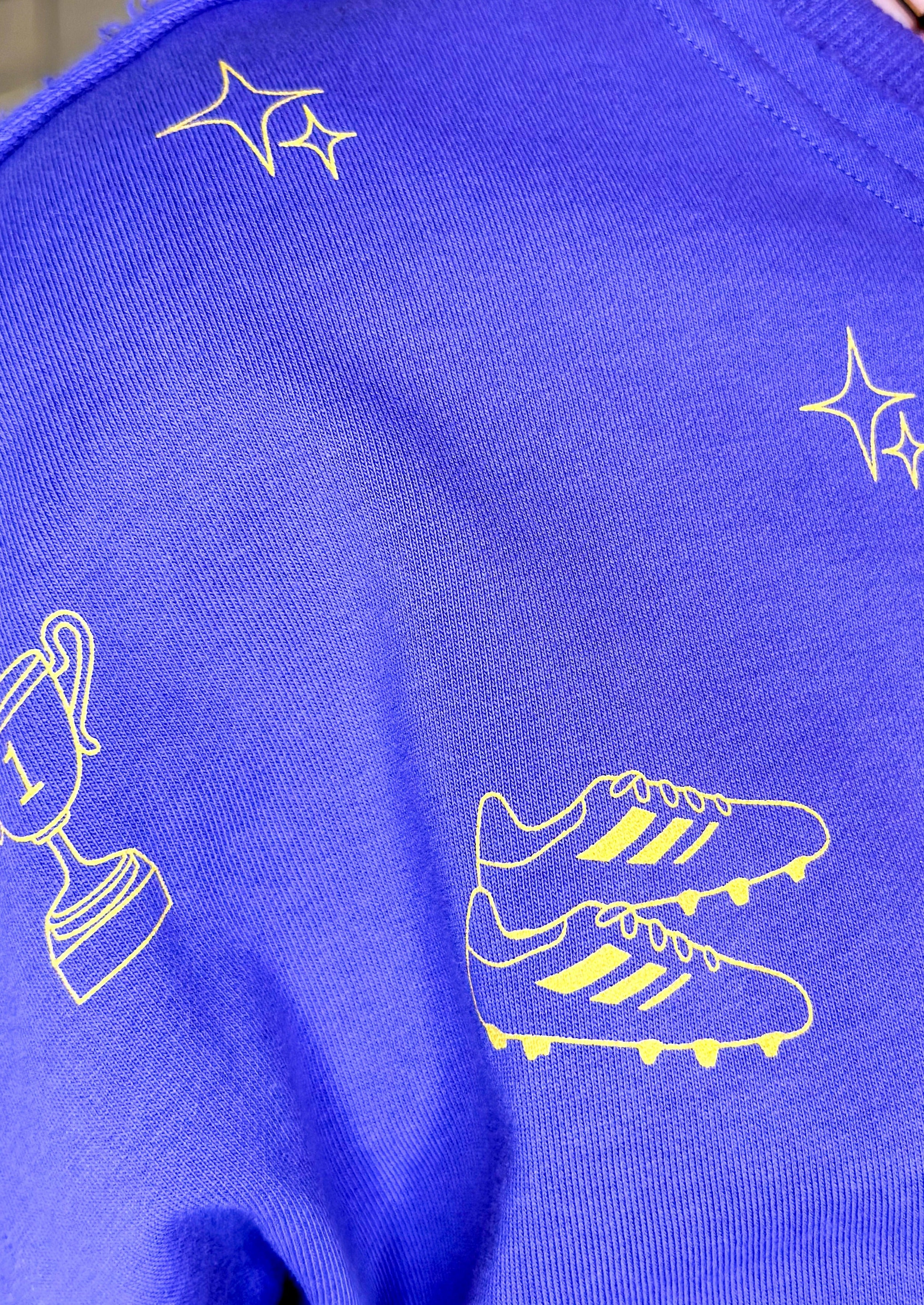 purple top with yellow football themed graphics - unfinished hem, dropped shoulder with folded cuff