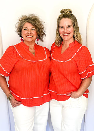 Dark coral short sleeve blouse with puff sleeves, split V-neckline, textured fabric, contrast white stripe trim detailing.