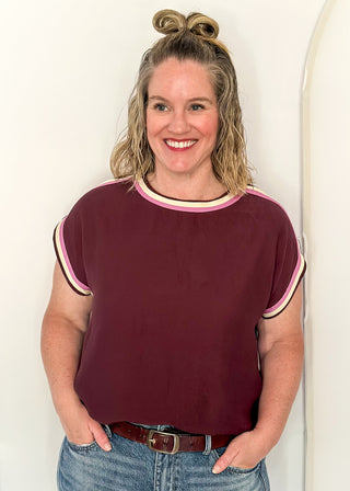 woman standing in Merlot top with pink and white contrast detail. 