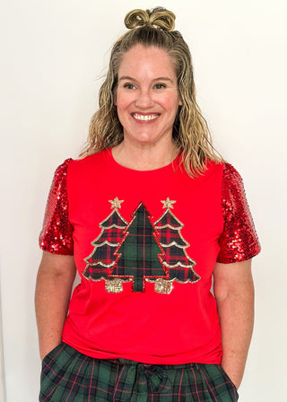 Woman wearing a red shirt with Christmas tree design and sequin sleeves against a white background