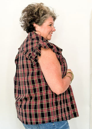 side view of woman wearing a dark navy plaid top with flutter sleeves 