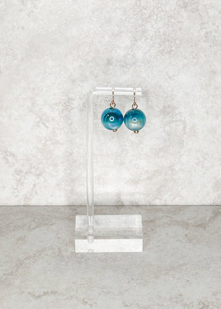 Pair of blue bead fish hook earrings on a clear stand against a light gray marble background